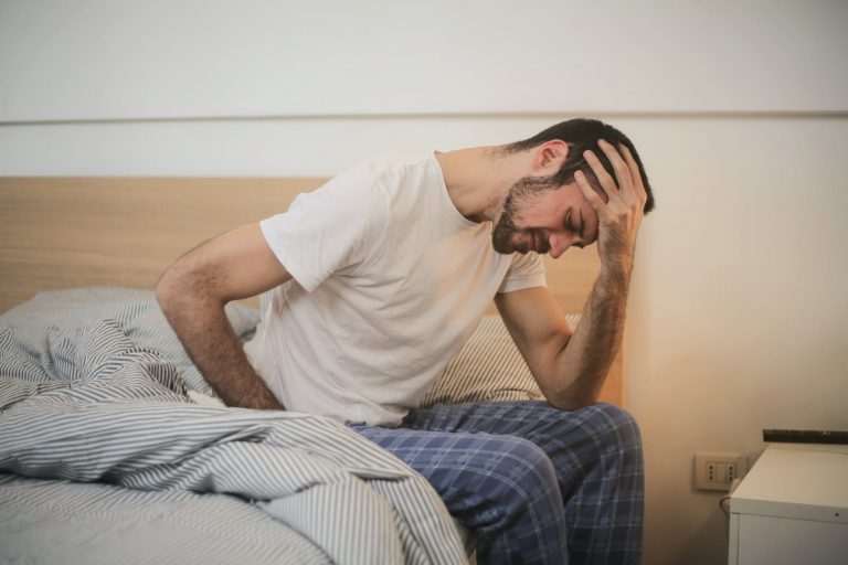 Man holds his head while sitting in bed.