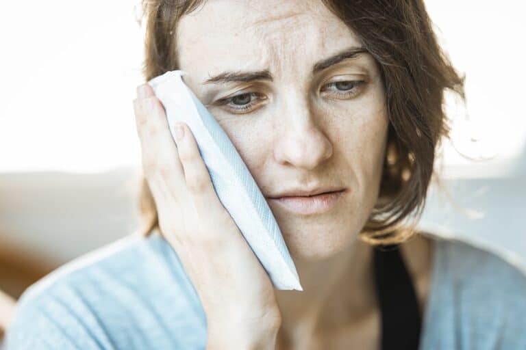 A woman holds an ice pack up to her face to relieve TMJ pressure.