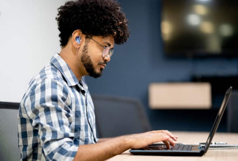 Side view of man wearing hearing aids working on laptop at office