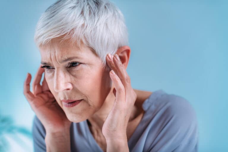 Woman holding ears experiencing tinnitus