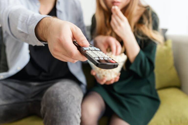 Couple watching TV and pointing remote.